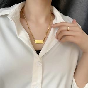 Gold titanium steel necklace with asymmetric chain and rectangular engraved pendant on model