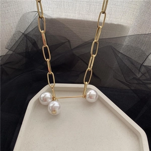 Close-up of golden paperclip chain necklace with three large round white pearls on a tray