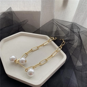 Detailed macro of a gold paperclip link necklace with three elegant white pearls