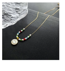 Detail of gold chain necklace with colorful beads and a white enamel smiley face charm