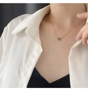 Primer plano de un collar dorado con colgante de carita verde en una modelo