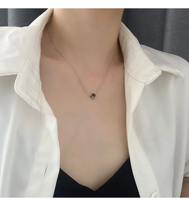 Primer plano de una cadena de plata minimalista con un colgante de cara sonriente negra