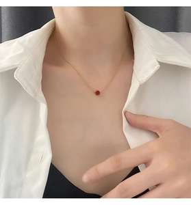Primer plano de un delicado collar de titanio dorado con un colgante redondo rojo