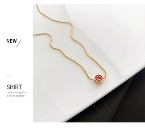 Detalle de un collar de cadena de serpiente dorada con un colgante de cara sonriente roja