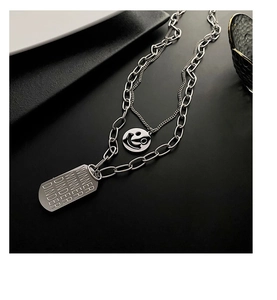 Macro detail of silver titanium steel layered necklace with smiley and engraved tag