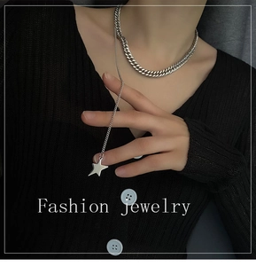 Detail of silver star pendant on a chunky curb chain necklace worn over black knitwear