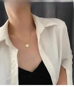 Détail d'un collier doré avec pendentif en nacre blanche et lettre B porté par un mannequin