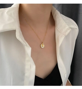 Détail macro du collier amulette doré avec nacre blanche porté par un mannequin