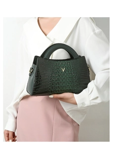 Detail of dark green crocodile pattern handbag with golden V-shaped metal logo on front