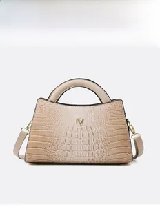 Detail view of beige crocodile embossed handbag with a metallic golden V logo decoration