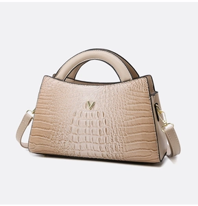 Detail of beige crocodile embossed handbag with V-shaped gold logo and textured PU leather