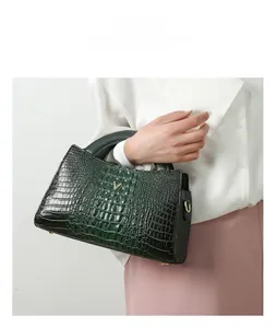 Detail of dark green handbag with crocodile texture and gold V-shaped metal logo hardware