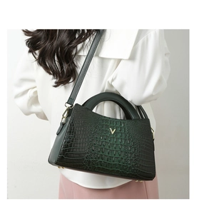 Detail of dark green crocodile embossed handbag with golden V logo and adjustable strap