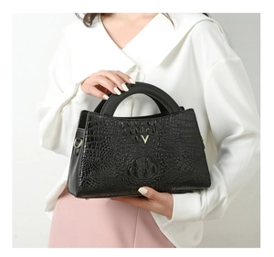 Detail of black crocodile texture handbag with gold V metal logo and sturdy top handle