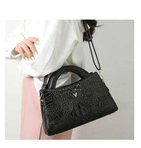 Detail of black crocodile-embossed leather handbag with V-shaped gold hardware and handles