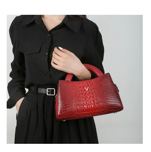 Detailed view of red crocodile-patterned handbag with gold V-logo on glossy surface