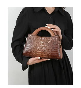 Detail of dark brown crocodile embossed tote bag featuring a metallic V-shaped logo accent