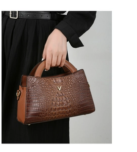 Detail of brown crocodile pattern handbag featuring a gold V-shaped logo and metallic hardware