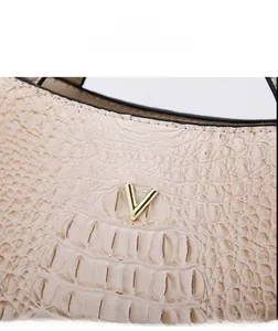 Detail view of beige crocodile embossed leather bag with gold V logo emblem