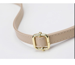 Detailed macro view of the beige textured leather strap with gold buckle and white stitching