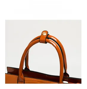 Detail of orange tote bag showing round handle, fine stitching and gold-tone metal hardware