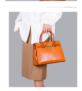 Detail of orange embossed crocodile texture handbag with gold twist lock hardware