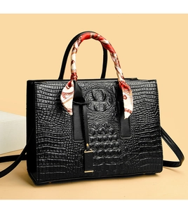 Dettaglio della borsa nera a coccodrillo con foulard decorativo in seta rossa sul manico