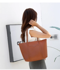 Borsa tote marrone a grana litchi con tasca frontale indossata in un ambiente minimalista