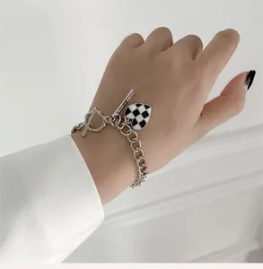 Détail d'un bracelet en chaîne argentée avec pendentif damier en cœur et fermoir à bascule