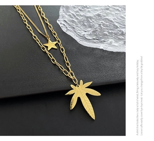 Detail showing a layered gold titanium necklace with star and leaf charms on textured glass