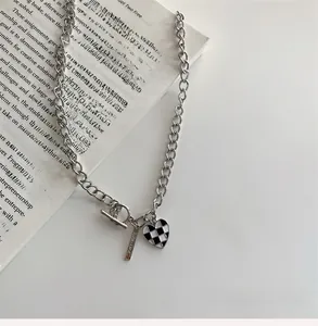 Détail du collier à chaîne argentée avec pendentif cœur en damier et fermoir en T