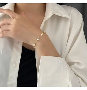 Vue détaillée d'un bracelet doré ondulé orné de cinq zircons blancs portés au poignet féminin