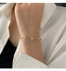 Détail d'un bracelet doré ondulé serti de zircons porté au poignet sur fond de chemise