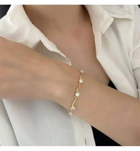 Gros plan d'un bracelet doré ondulé avec trois zircons sur une manche blanche