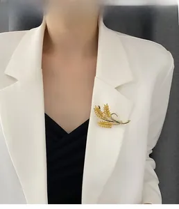 Detailed close-up of a golden wheat ear brooch pinned on a white suit blazer
