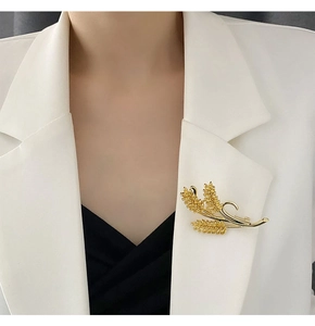 Detailed view of a golden wheat stalk brooch with sparkling crystals on a white blazer