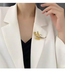 Detail of zircon-encrusted gold wheat ear brooch pinned on a white formal suit lapel