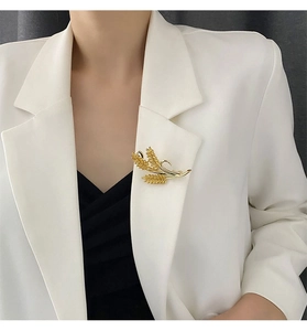 Detail of a gold wheat stalk brooch featuring zircon inlays on a white suit jacket