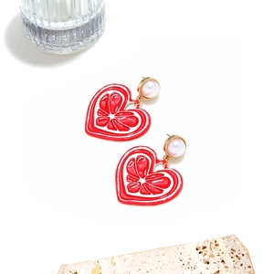 Détail de boucles d'oreilles cœur rouge avec perle sur fond de pierre blanche
