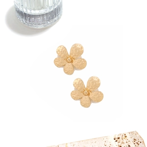 Macro shot of gold alloy flower earrings with unique hammered texture on white background