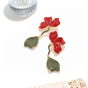 Détail macro de boucles d'oreilles fleurs en émail rouge peint à la main et tiges dorées