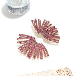 Macro shot of fan-shaped gold earrings with pink rhinestones on a beige stone
