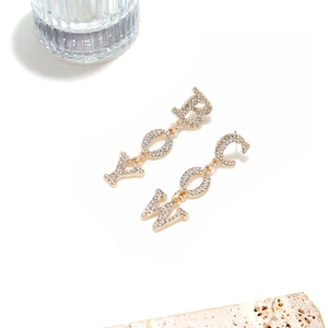 Close-up of gold COWBOY lettering earrings with rhinestones on a stone base