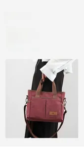 Détail du sac bandoulière en toile bordeaux avec poches multiples et écusson logo en cuir