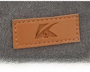 Gros plan d'un patch logo en cuir marron cousu sur un sac en toile gris foncé