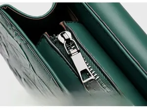Detailed macro of the high-quality silver alloy zipper on a dark green crocodile pattern bag