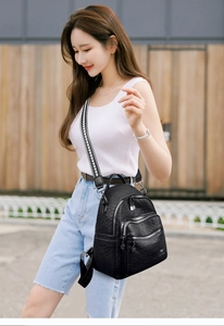 Detailed view of black litchi leather backpack with multiple zippers and woven strap