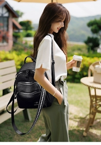 Detail of black faux leather backpack featuring gold kangaroo logo and jacquard strap