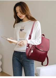 Close-up of wine red textured leather backpack featuring metal kangaroo logo and side pocket