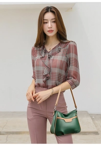 Outdoor lifestyle shot of a green and brown leather crossbody bag with kangaroo logo
